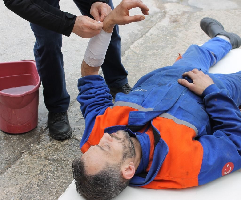 Injured worker receiving first aid on-site with arm bandage applied.
