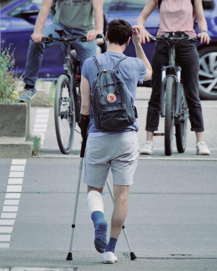 A person with a leg injury using crutches on a street. Encounter with cyclists in an urban setting.