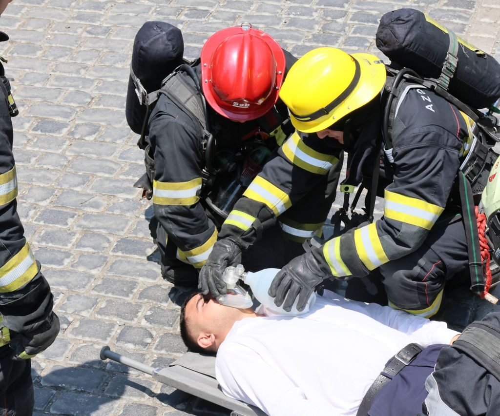 Firefighters provide CPR to an injured man using a bag valve mask on a cobblestone street.
