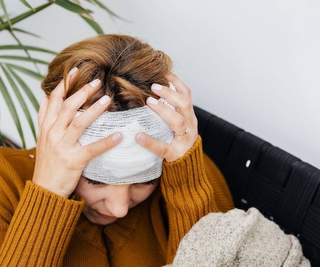 Woman with head injury holding her head in pain indoors.