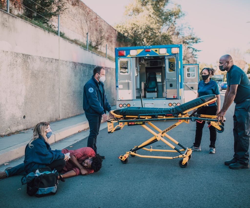 Team of paramedics assists a patient on roadside near an ambulance, showcasing emergency response.