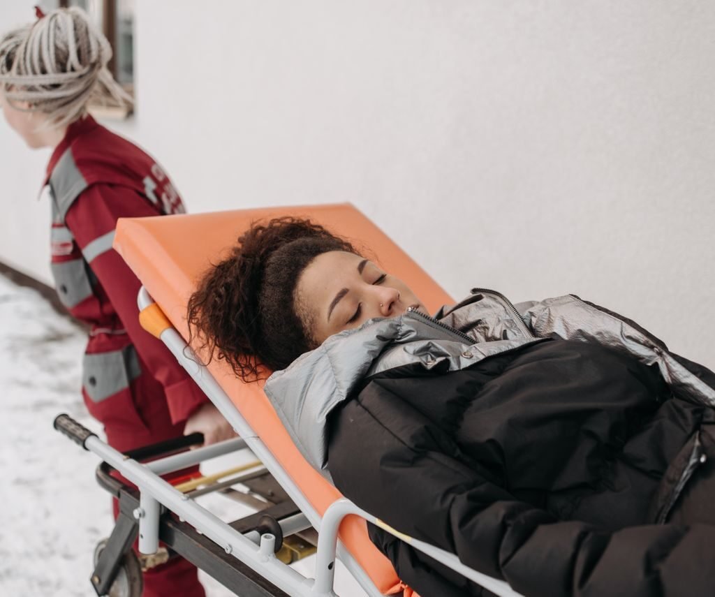 Medical personnel assisting a patient on a stretcher outdoors in a snowy setting.