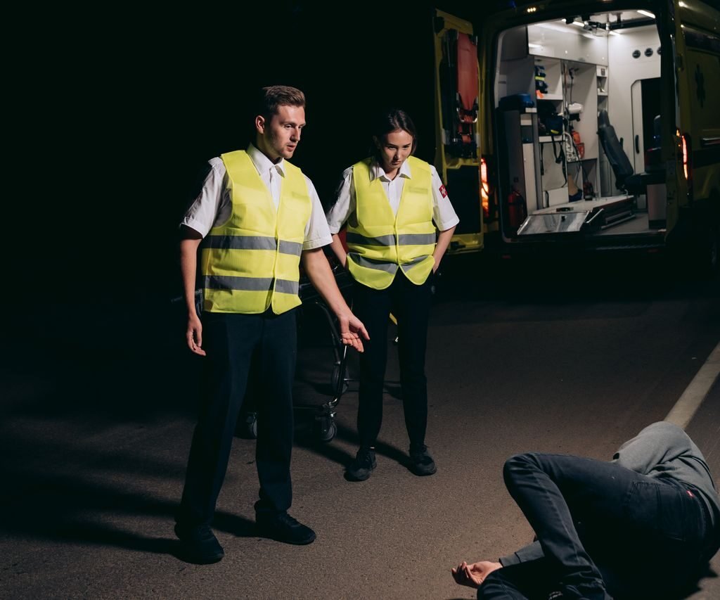 Paramedics assist a patient on a dimly lit street, showcasing emergency response at night.