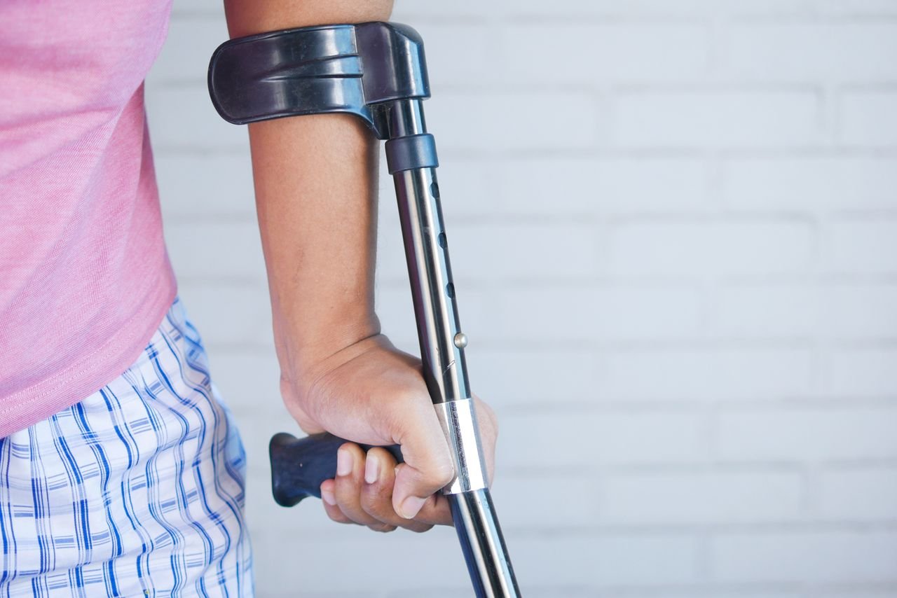 Crafting Captivating Headlines: Your awesome post title goes here Close-up of a person in a pink shirt using a crutch for support indoors against a brick wall.